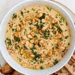 Peanut butter hummus in a bowl topped with peanuts, herbs, sesame seeds and crostini on the side.