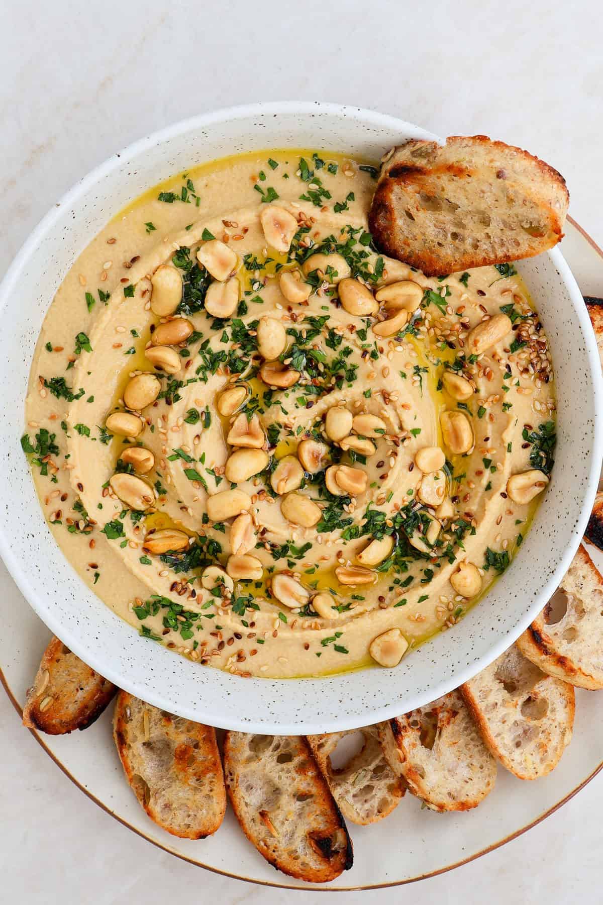 Peanut butter hummus in a bowl topped with peanuts, herbs, sesame seeds and crostini dipped in.