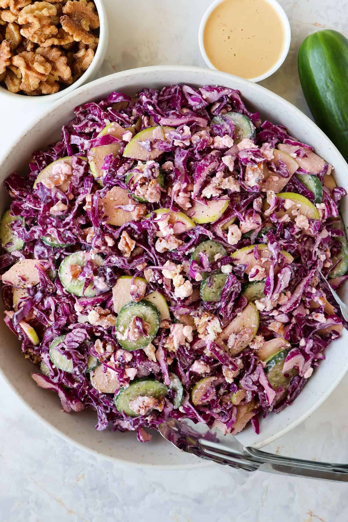 Red cabbage salad in a bowl with tongs.