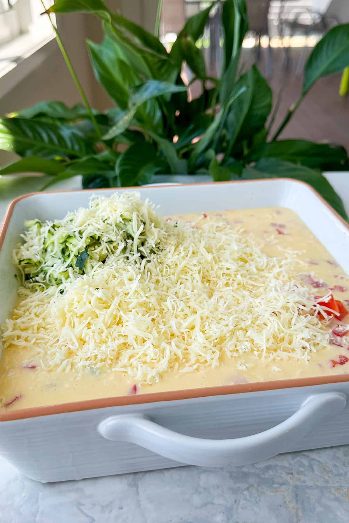 Egg mixture poured into a dish with grated zucchini, capsicum and cheese.