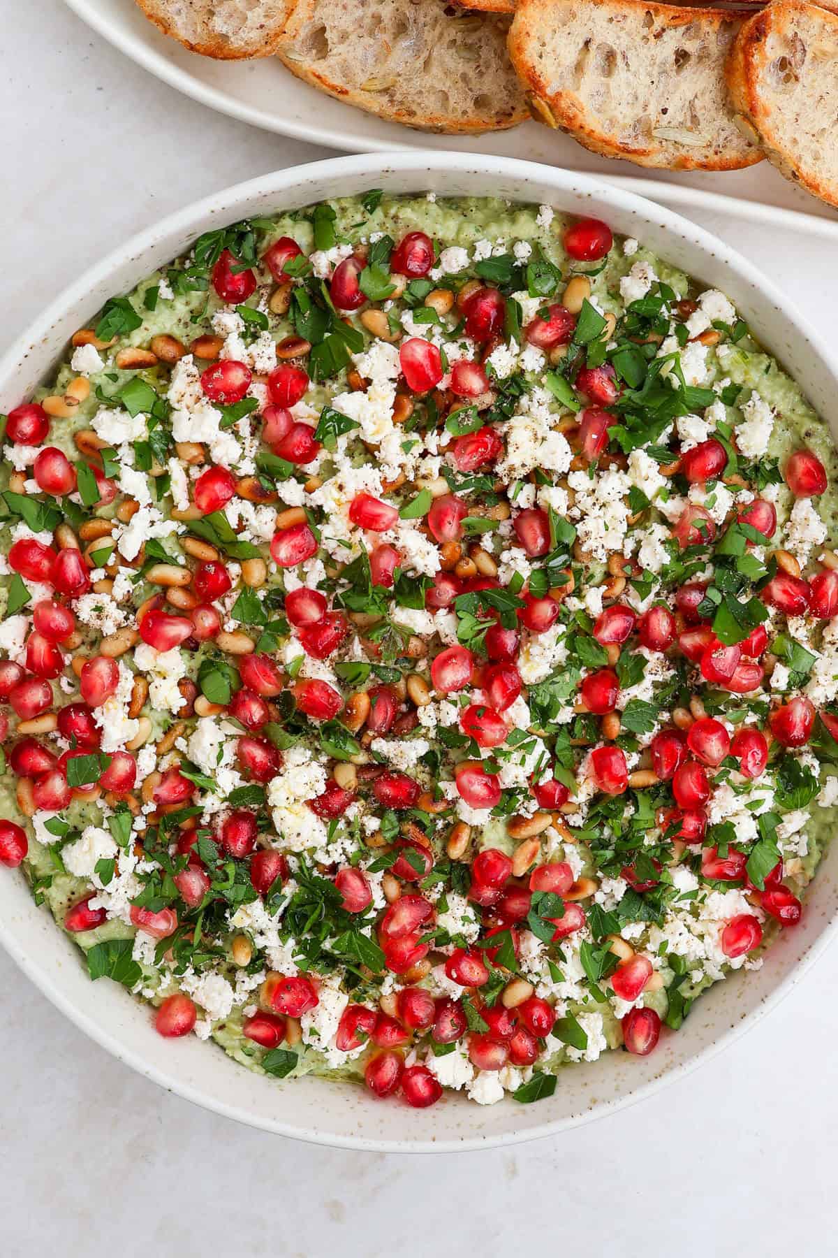 Green pea dip garnished with pomegranate, feta, herbs and pine nuts.