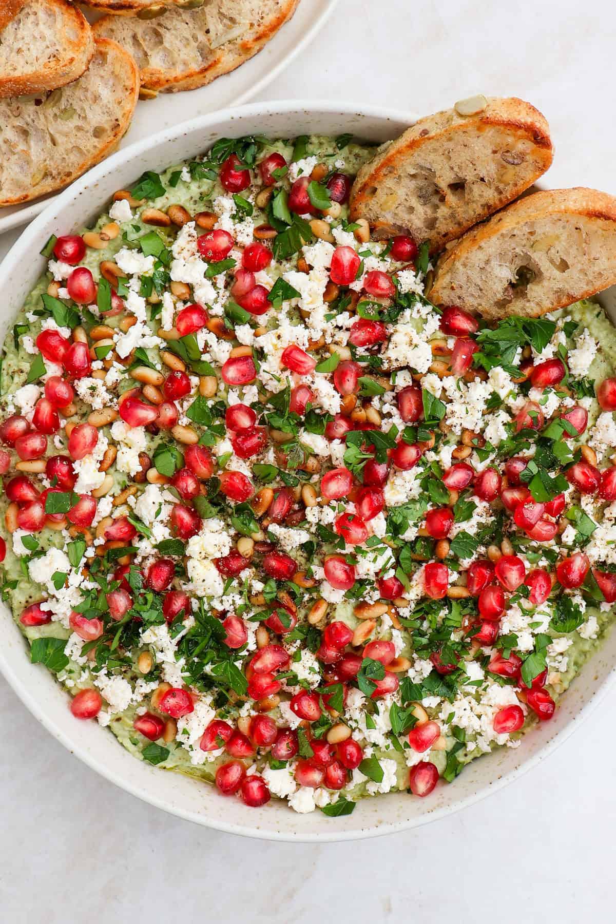 Green pea dip garnished with pomegranate, feta, herbs and pine nuts.