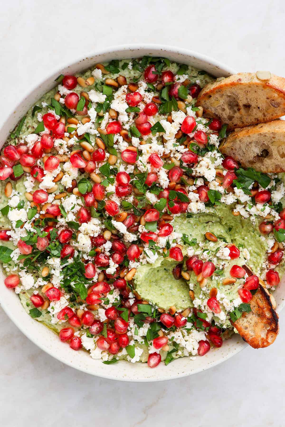 Green pea dip garnished and scooped up with crostini bread tp see inside.