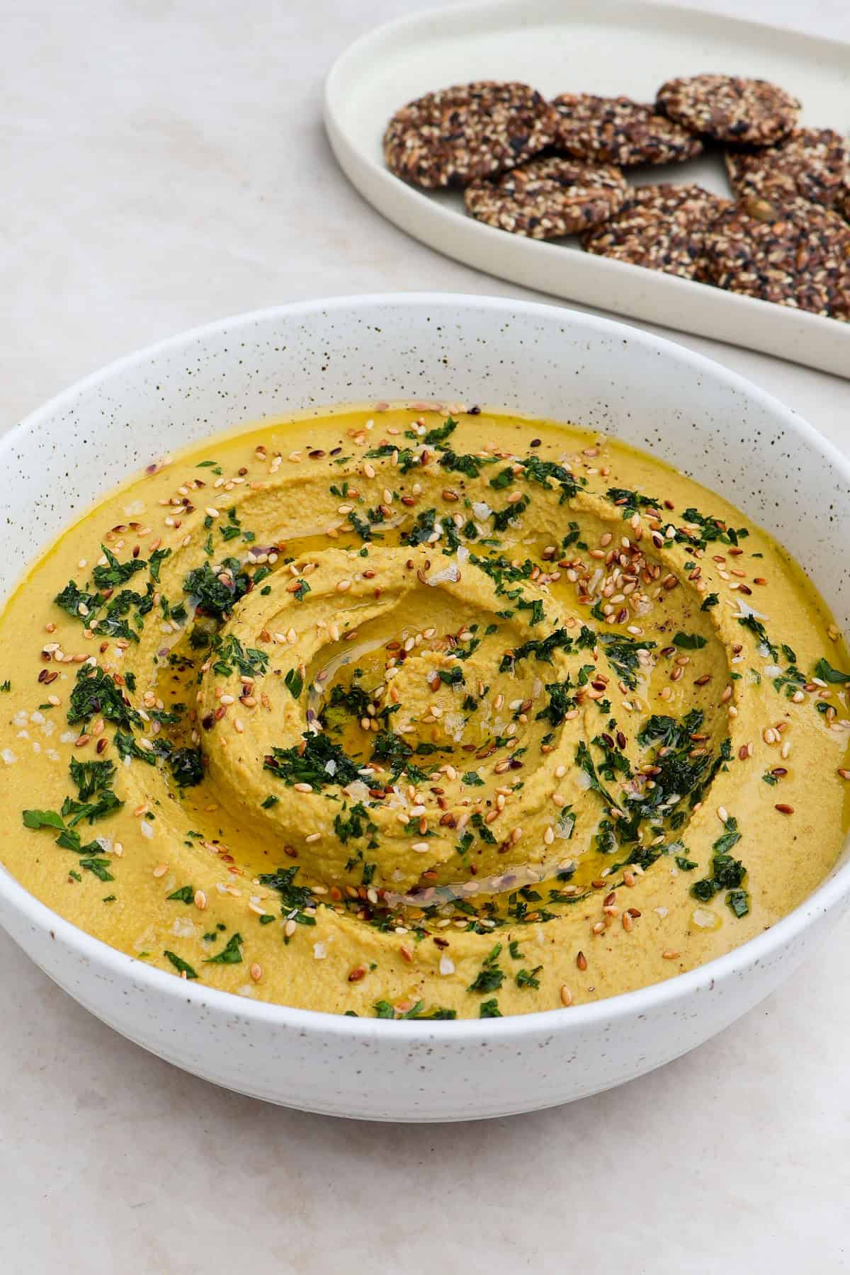 Side shot of the golden lentil hummus with crackers in the background.