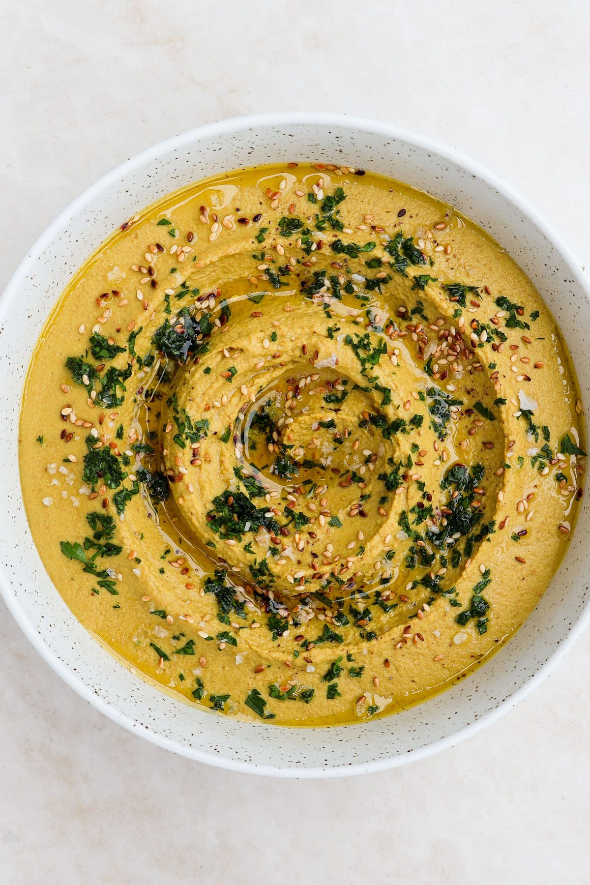 Hummus served in a bowl with herbs, sesame seeds and olive oil.