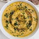 Lentil hummus in a bowl with chopped herbs and sesame seeds on top.
