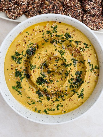 Lentil hummus in a bowl with chopped herbs and sesame seeds on top.
