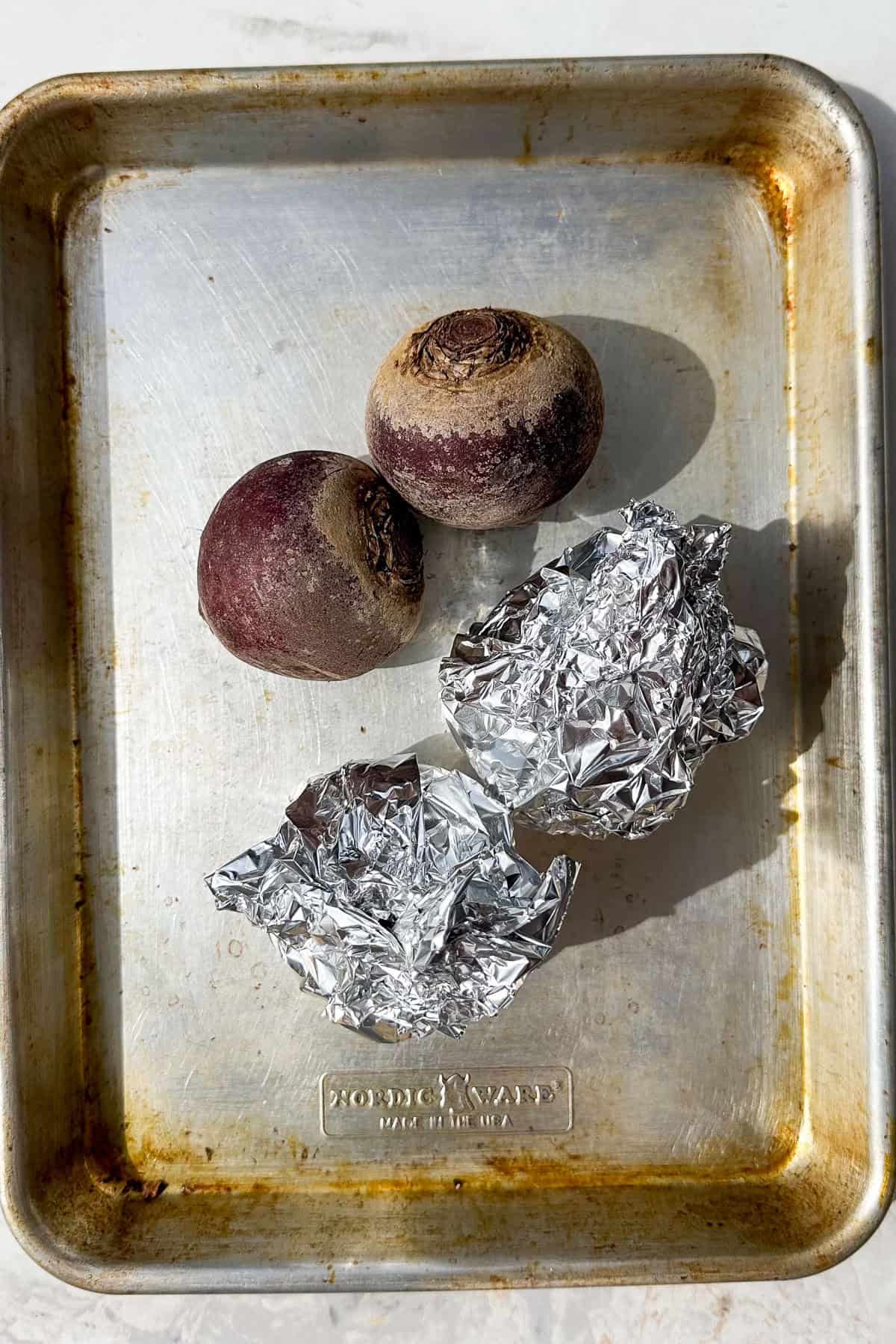 Beetroots covered with foil on a tray.