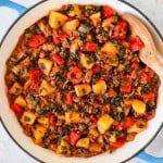 Ground beef, potatoes and peppers in a skillet with a wooden spoon.