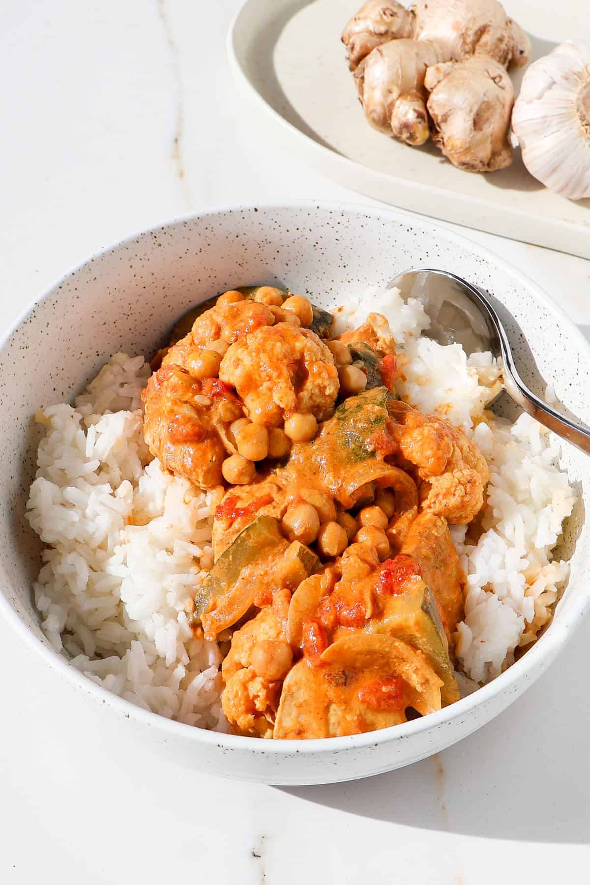 Side shot of chicken and chickpea curry served over rice in a bowl.