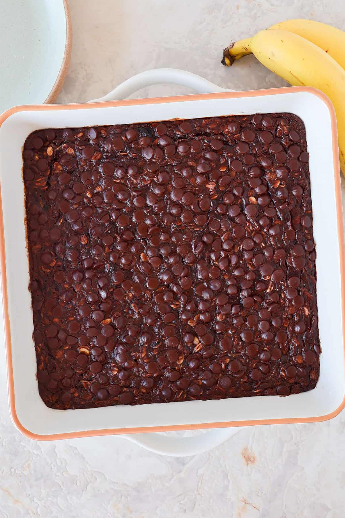 Chocolate baked oatmeal in a dish with a banana and plate on the sides.