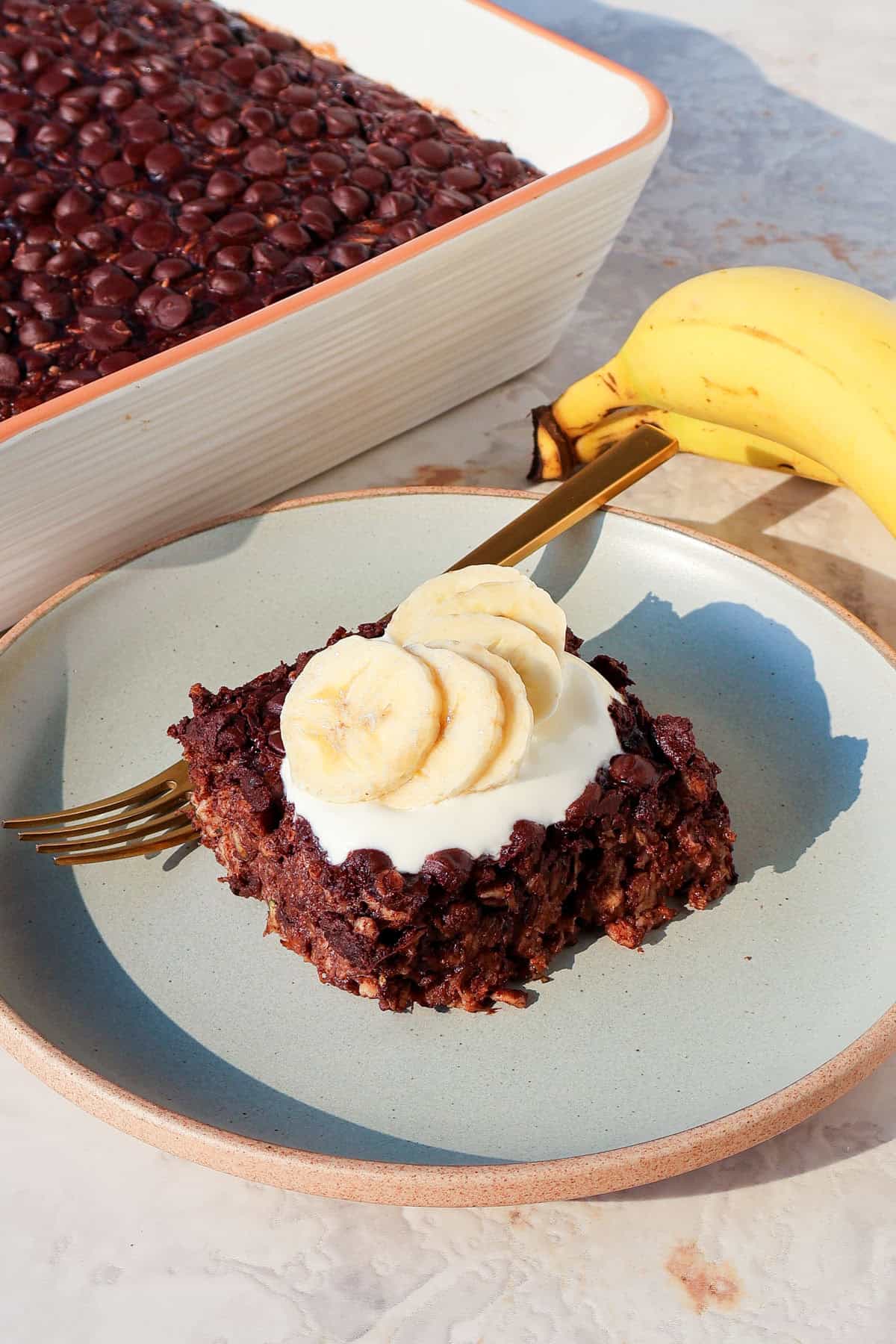 Side shot of the chocolate baked oatmeal topped with yoghurt, bananas and a fork.